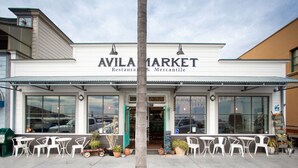 A storefront with the name "AVILA MARKET" and a sign indicating it is a restaurant and mercantile. There are outdoor tables and chairs in front of the building.