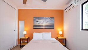 A bedroom with a large bed, two bedside tables with lamps, an air conditioning unit, and a window. - Balcones del Pacifico 21, pool, and Private rooftop access in the heart of town! (Tamarindo)