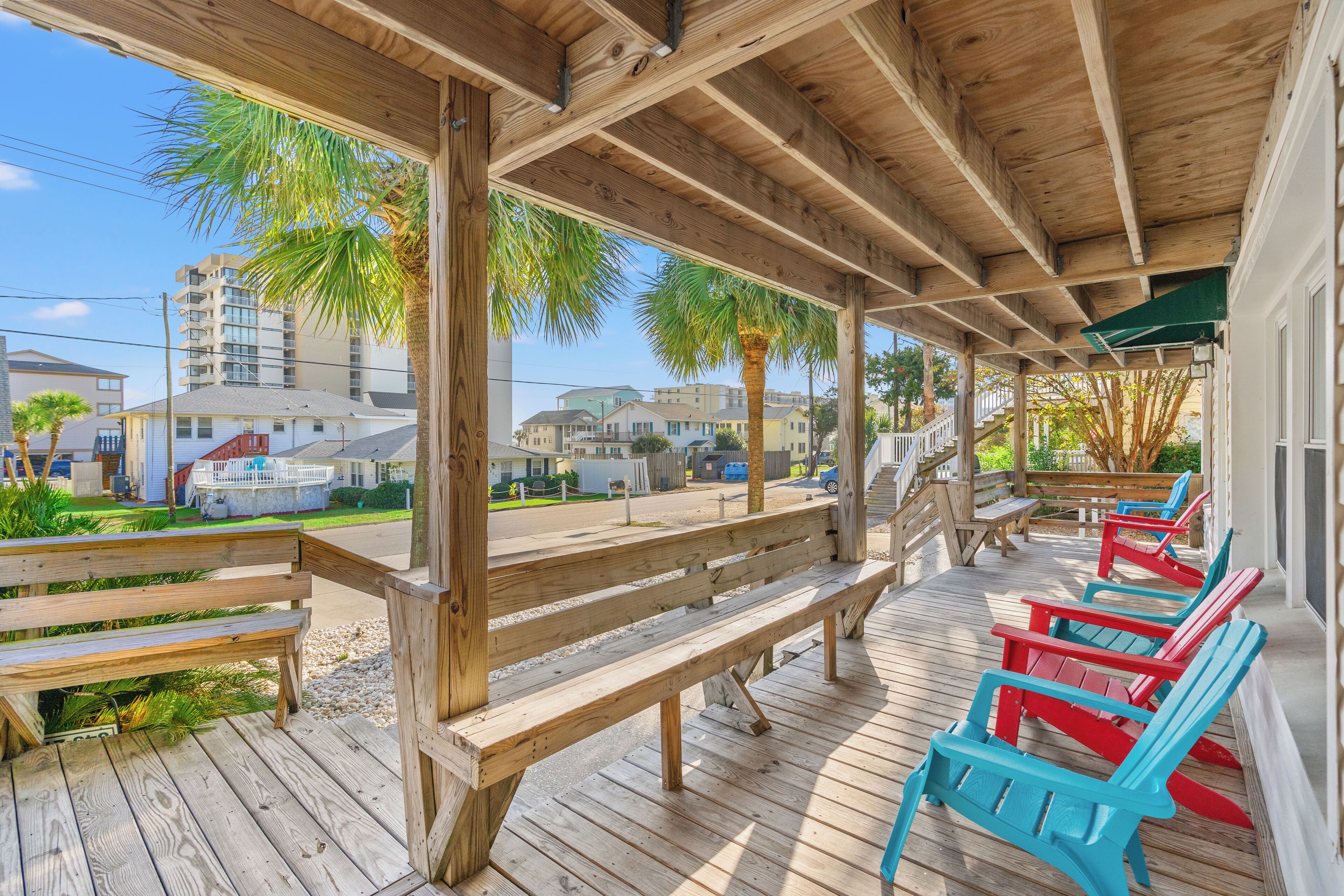 A wooden deck with benches and colorful Adirondack chairs, overlooking a residential area with houses and a palm tree.