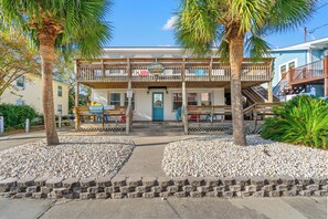 Un bâtiment situé en bord de mer, doté d’une terrasse en bois et d’une enseigne indiquant « Bar et grill en bord de mer ».