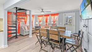 A spacious living area with a dining table, chairs, and a staircase with orange curtains. - Newly Refurbished Beach House w/Pool & Hot Tub + Free Attraction Tickets! (North Myrtle Beach)
