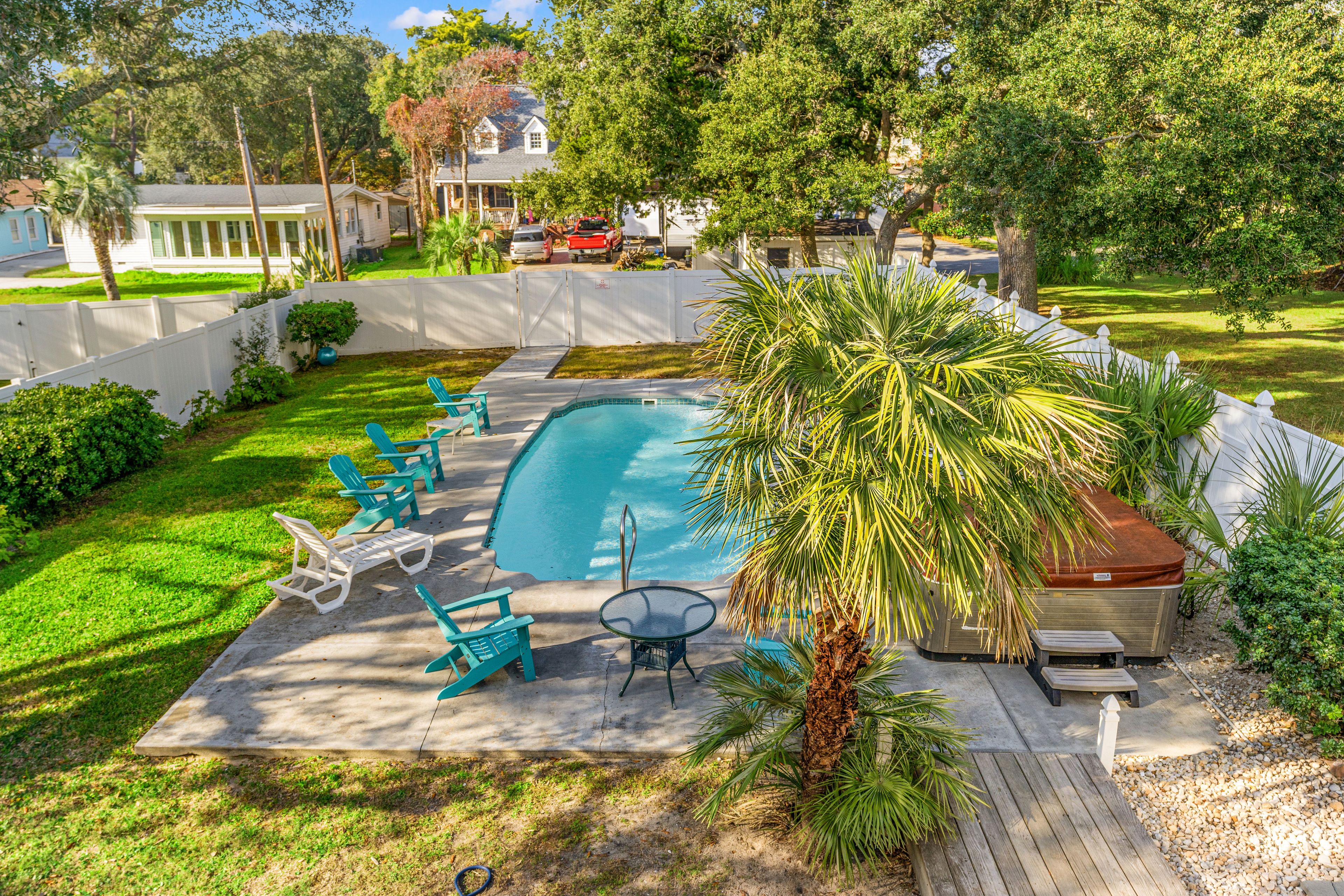 A backyard with a swimming pool, green chairs, a hot tub, and a wooden deck.