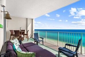 A balcony with a view of the ocean, furnished with a sofa, chairs, and a table.