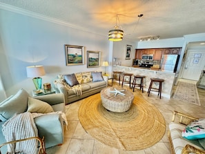 A living room with a sofa, a coffee table, a lamp, and a kitchen in the background.