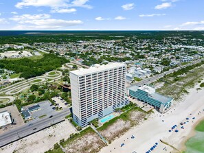 A high-rise hotel with multiple floors, a swimming pool, and a beach area.