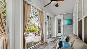 Un portico riparato con un divano color beige, tende color beige e una ventola a soffitto.