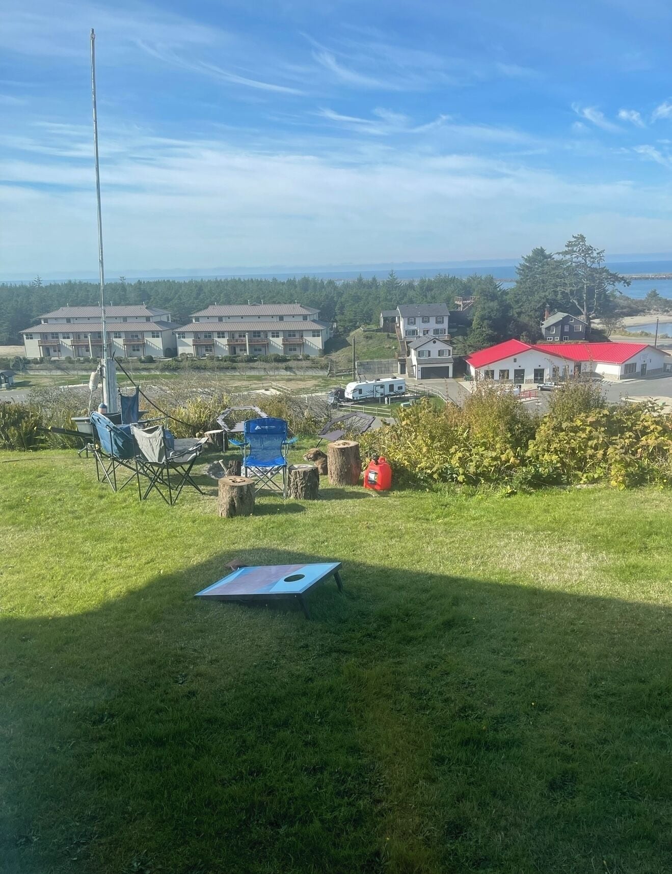 Une zone herbeuse avec une structure métallique, une chaise pliante bleue et un bâtiment rouge en arrière-plan.