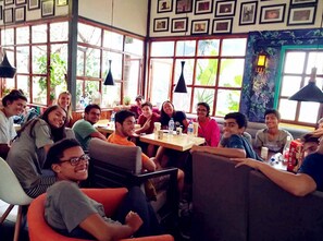 A group of people seated around a table in a room with large windows and framed pictures on the walls. - Upland International Youth Hostel (Kunming)
