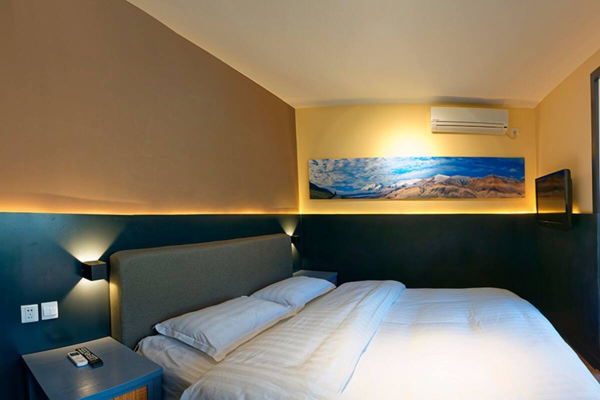 Ein Hotelzimmer mit Bett, Nachttisch, einem Bild an der Wand und einem Fenster mit Vorhängen.