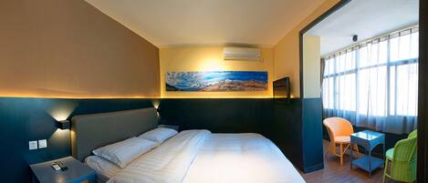 A hotel room with a bed, a nightstand, a painting on the wall, and a window with curtains.
