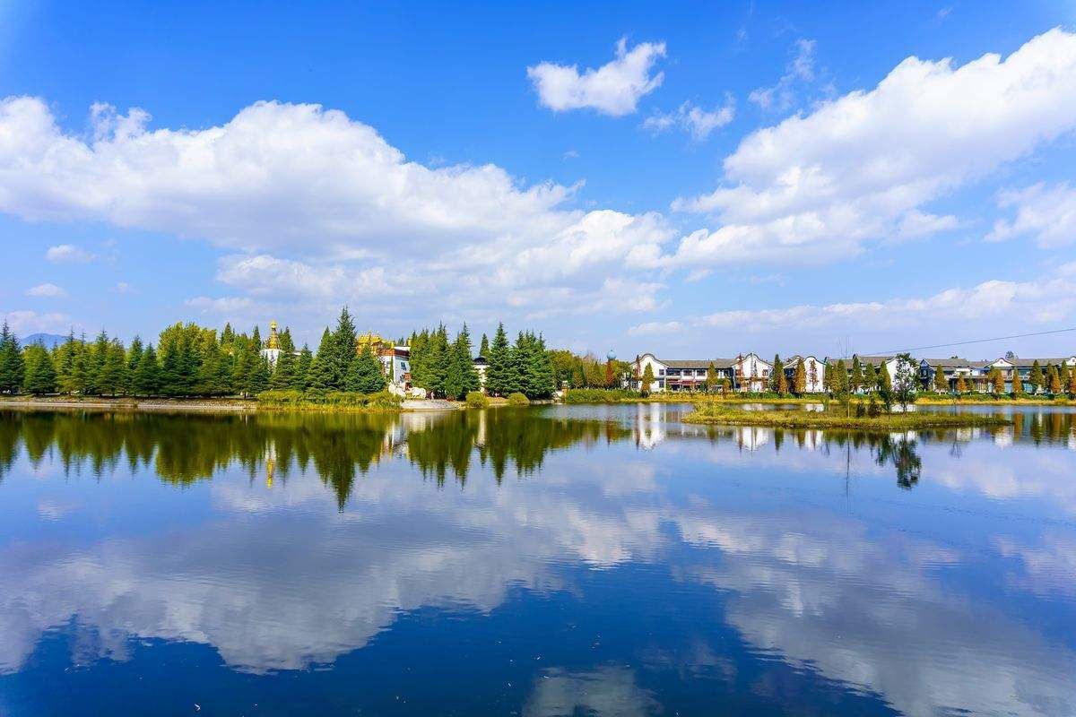 A calm lake with a reflection of the sky and trees, surrounded by residential buildings and a prominent church with a golden dome.
