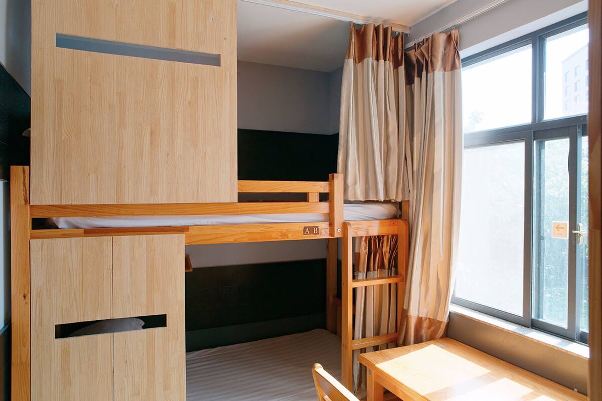 Ein Schlafraum im Schlafsaalstil mit Etagenbetten, einem Schreibtisch und einem Fenster mit Vorhängen.