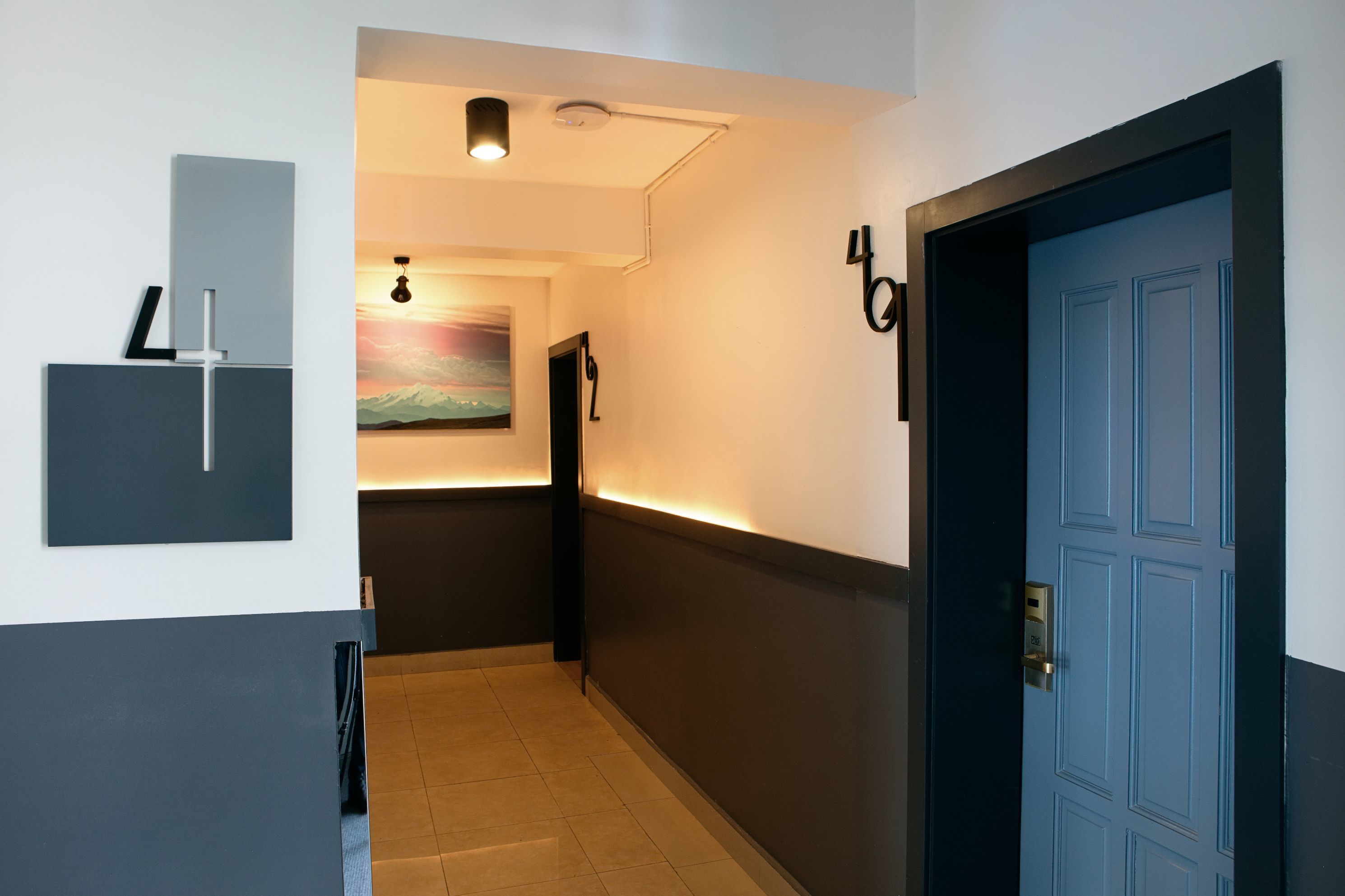 A hallway with a blue door, a wall-mounted light fixture, and a painting on the wall.