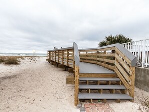 Una escalera de madera que lleva a una zona de playa con un sendero de arena y una valla blanca al fondo.