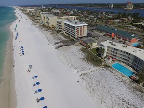An aerial view of a beachside hotel with multiple buildings, a sandy beach with umbrellas, and a clear view of the ocean.