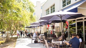 An outdoor café with tables and chairs under umbrellas, a building with a sign reading "Café & Bistro", and a tree-lined sidewalk.