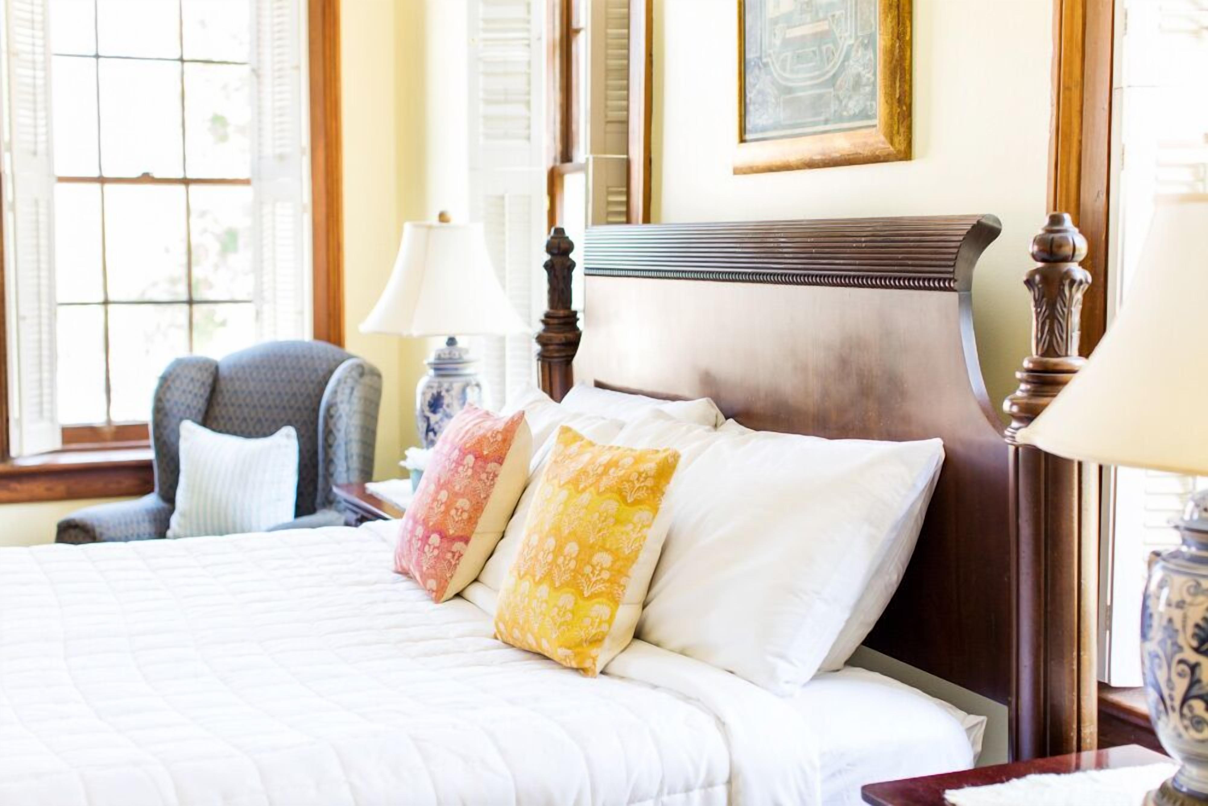 A neatly made bed with a wooden headboard, a chair, and a lamp on a bedside table.