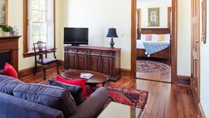 A room with a sofa, a television, a cabinet, and a bed with a patterned rug.