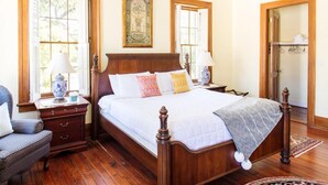 A bedroom with a wooden bed, two bedside tables, a chair, and a large window with shutters.