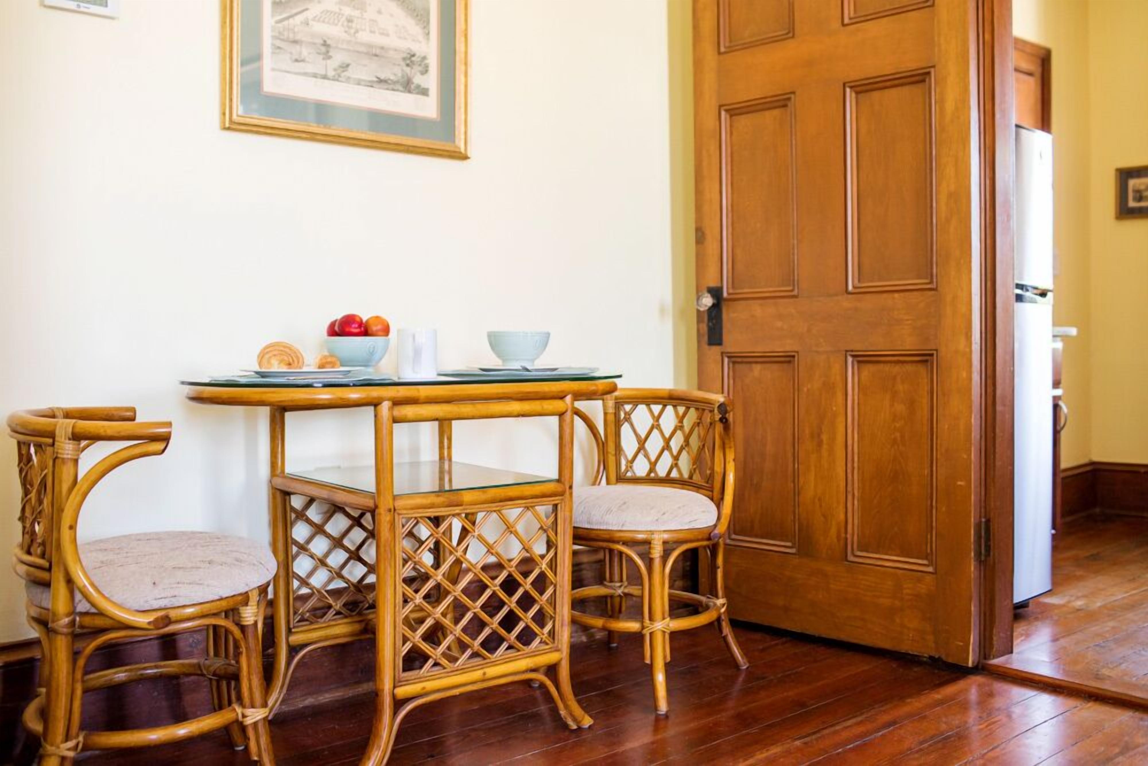Un coin repas avec une table en bois et des chaises en osier, un tableau encadré au mur et une porte en bois.