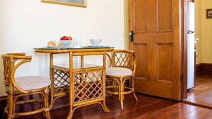 A dining area with a wooden table and wicker chairs, a framed picture on the wall, and a wooden door.