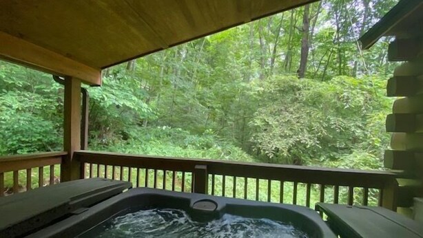 Een hottub met een houten terras en uitzicht op een bos.