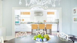 A modern kitchen with white cabinets, a stainless steel range hood, and a dining area with a table set for four. - Spend the Night in an Historical, Luxury Downtown Home by Lucky Savannah (Savannah)