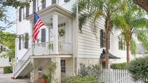 A white colonial-style house with a front porch, a flag, and a picket fence. - Spend the Night in an Historical, Luxury Downtown Home by Lucky Savannah (Savannah)