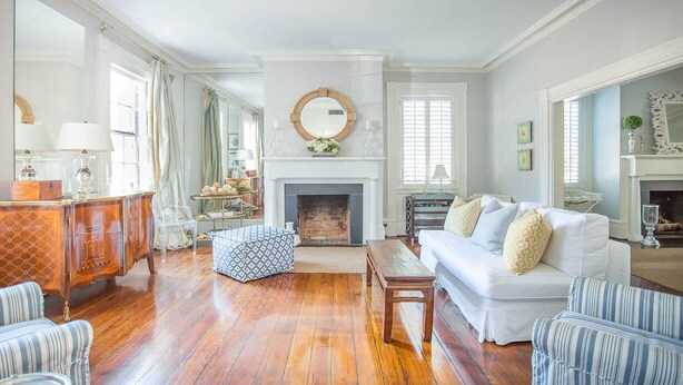 A spacious living room with a fireplace, a white sofa, striped chairs, and a wooden coffee table. - Spend the Night in an Historical, Luxury Downtown Home by Lucky Savannah (Savannah)