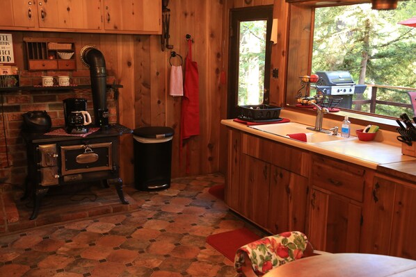 A rustic kitchen with wooden cabinets, a coffee maker, a sink, and a window with a view of trees. - Secluded "Hidden Heaven" Vintage Cabin on Strawberry Creek, Walk to town (Idyllwild)