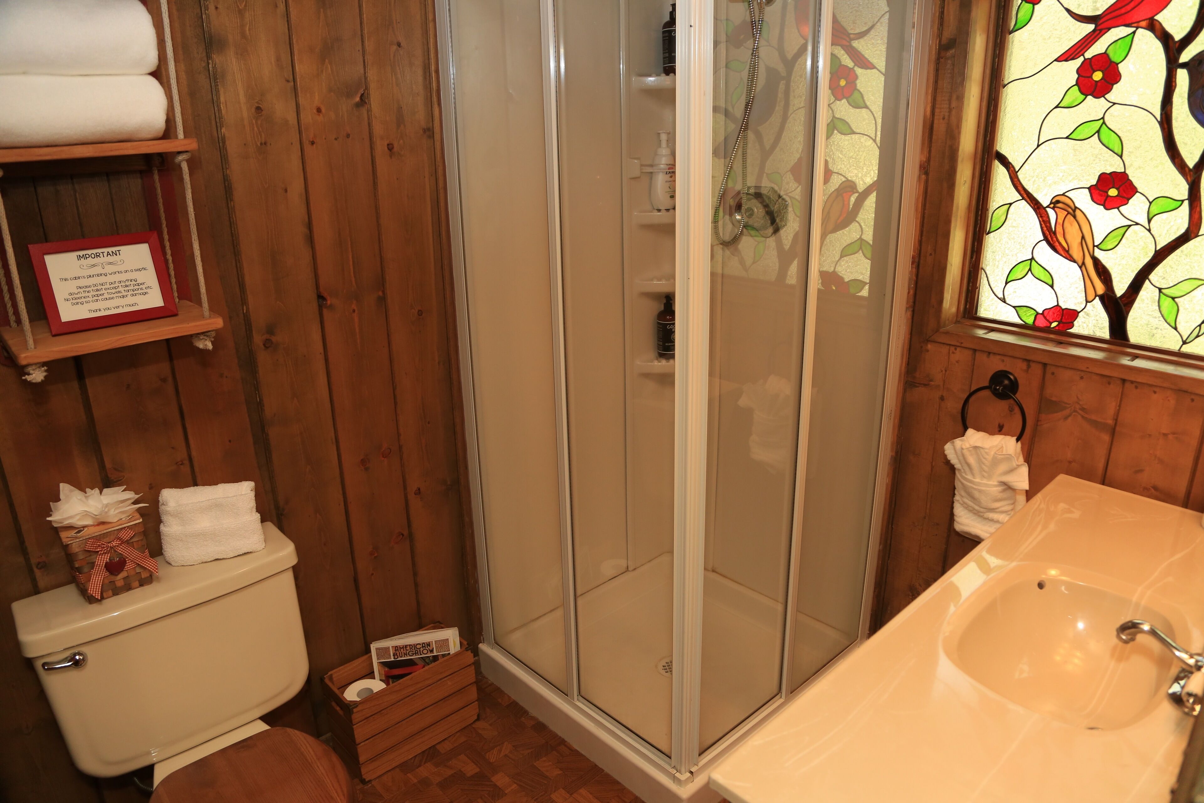 A wooden bathroom with a glass shower enclosure, a sink, and a stained glass window depicting birds.