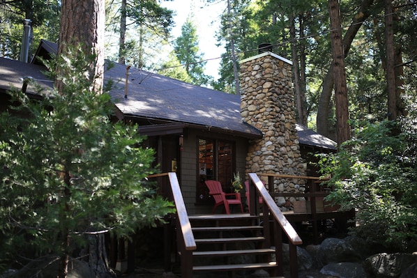Une cabane avec une cheminée en pierre, une terrasse en bois et des chaises rouges.