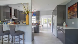 A modern kitchen with grey cabinets, a central island with bar stools, and a large window providing natural light. - Beach, Art District, Shopping, Restaurants! Best Spa in Delray! (Delray Beach)