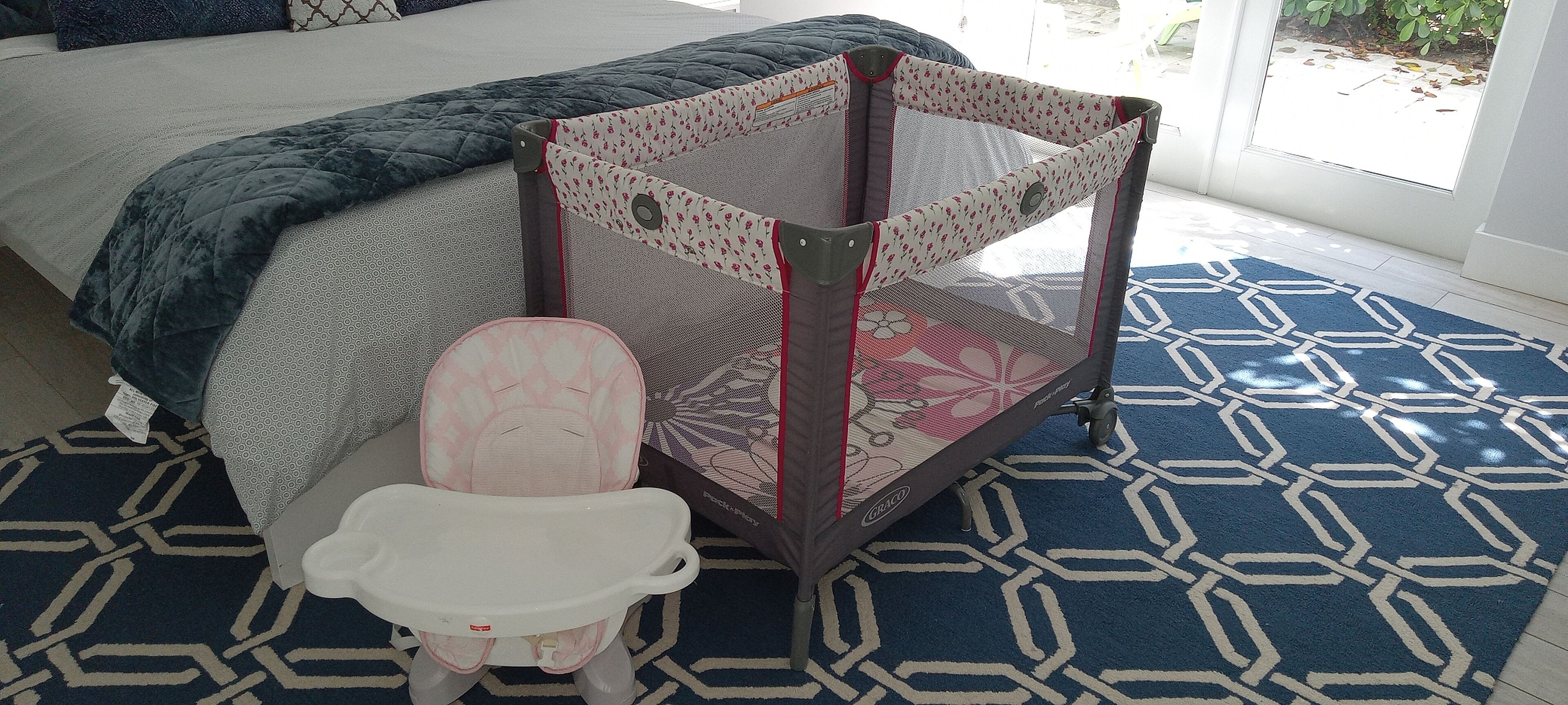 A room with a bed, a baby playpen, and a small white chair.