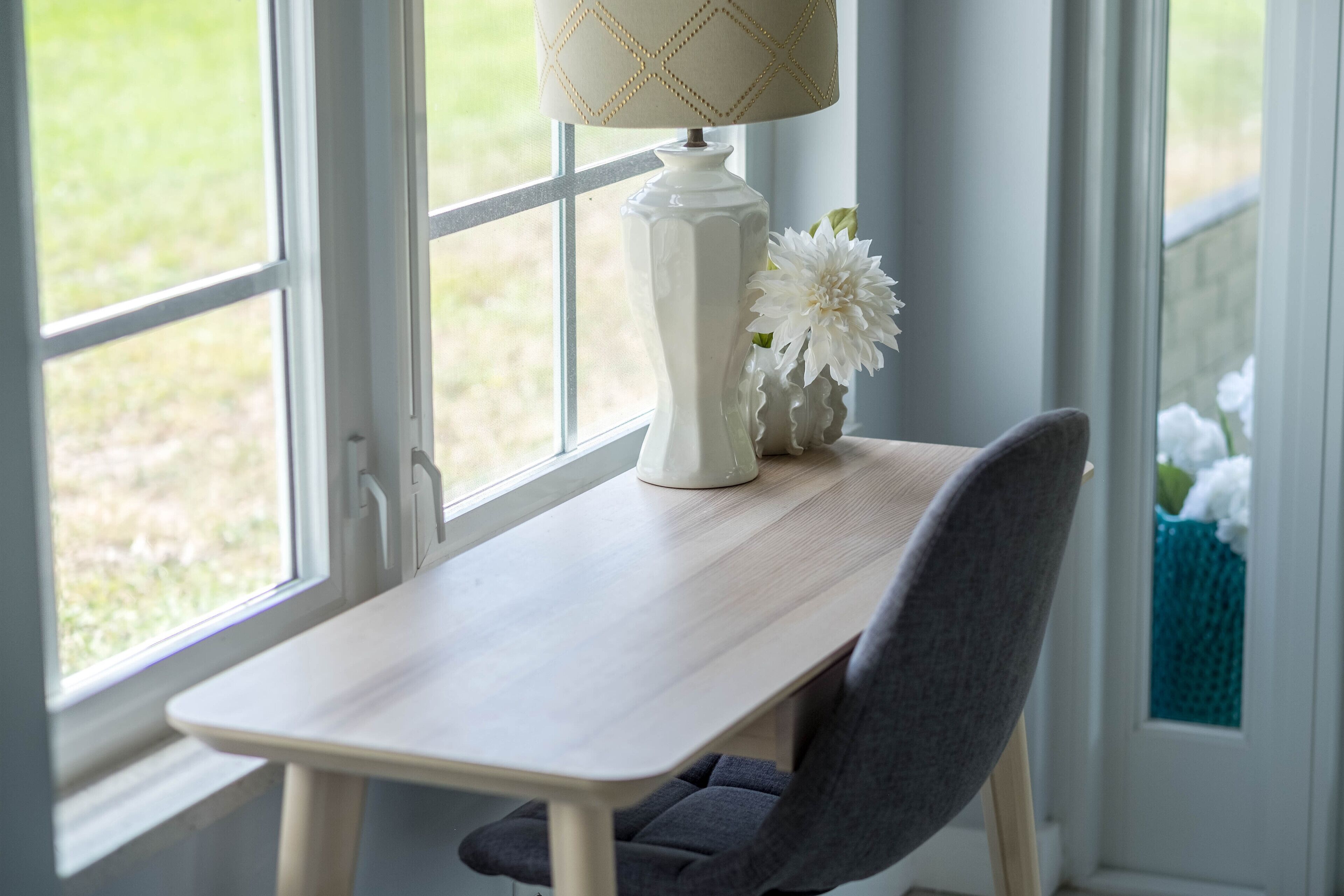 Une table avec une lampe et un vase de fleurs près d’une fenêtre.