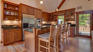 Una cocina amplia con armarios de madera, una isla central con taburetes de bar, electrodomésticos de acero inoxidable y vistas al exterior.