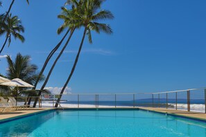 En klarblå pool med utsikt över havet och palmerna.