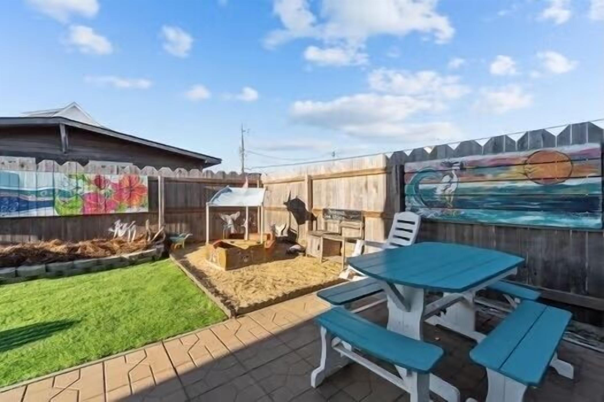 A backyard with a wooden fence, a barbecue grill, a picnic table, and a mural on the fence.