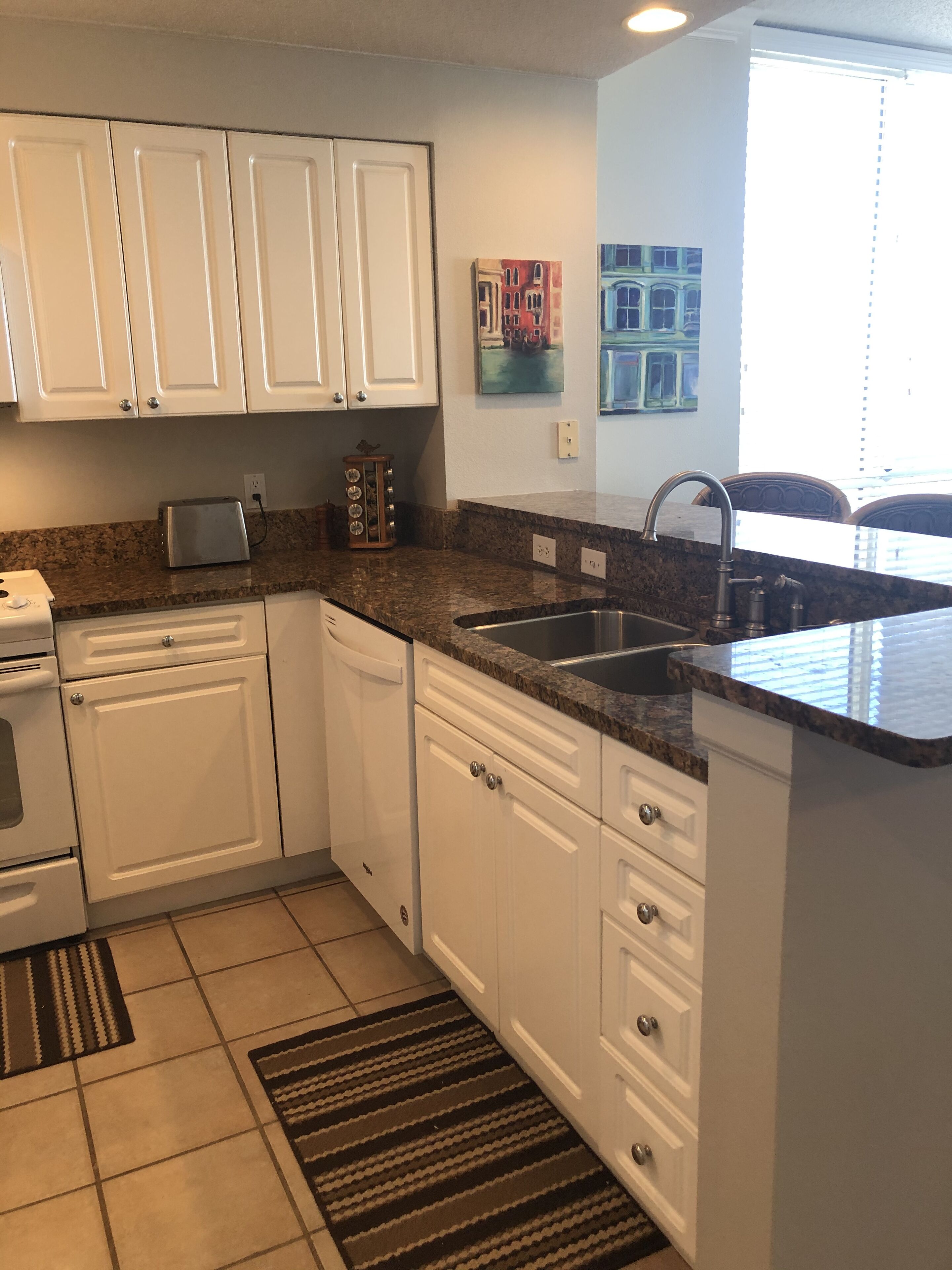 A modern kitchen with white cabinets, granite countertops, a double sink, and a toaster.