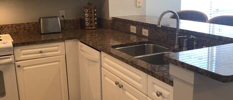 A modern kitchen with white cabinets, granite countertops, a double sink, and a toaster.