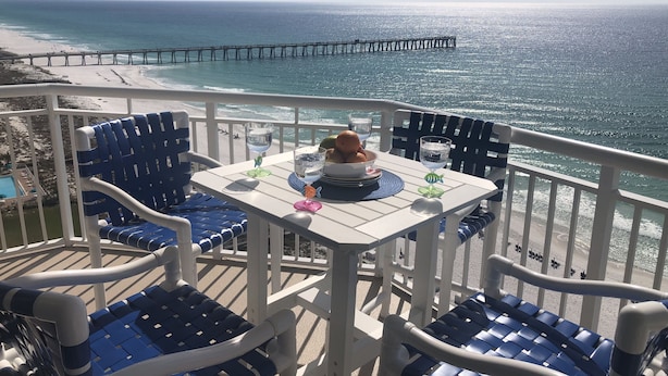 A balcony with a table set for two, overlooking a beach and a pier. - Wilson's Beach Dream: Gulf Front 5 Star 3BR 3Bath with Beach Service (Navarre)