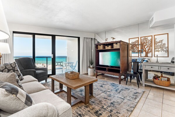 Un salon comprenant un canapé, une table basse, un téléviseur, un bureau et une vue sur la plage.