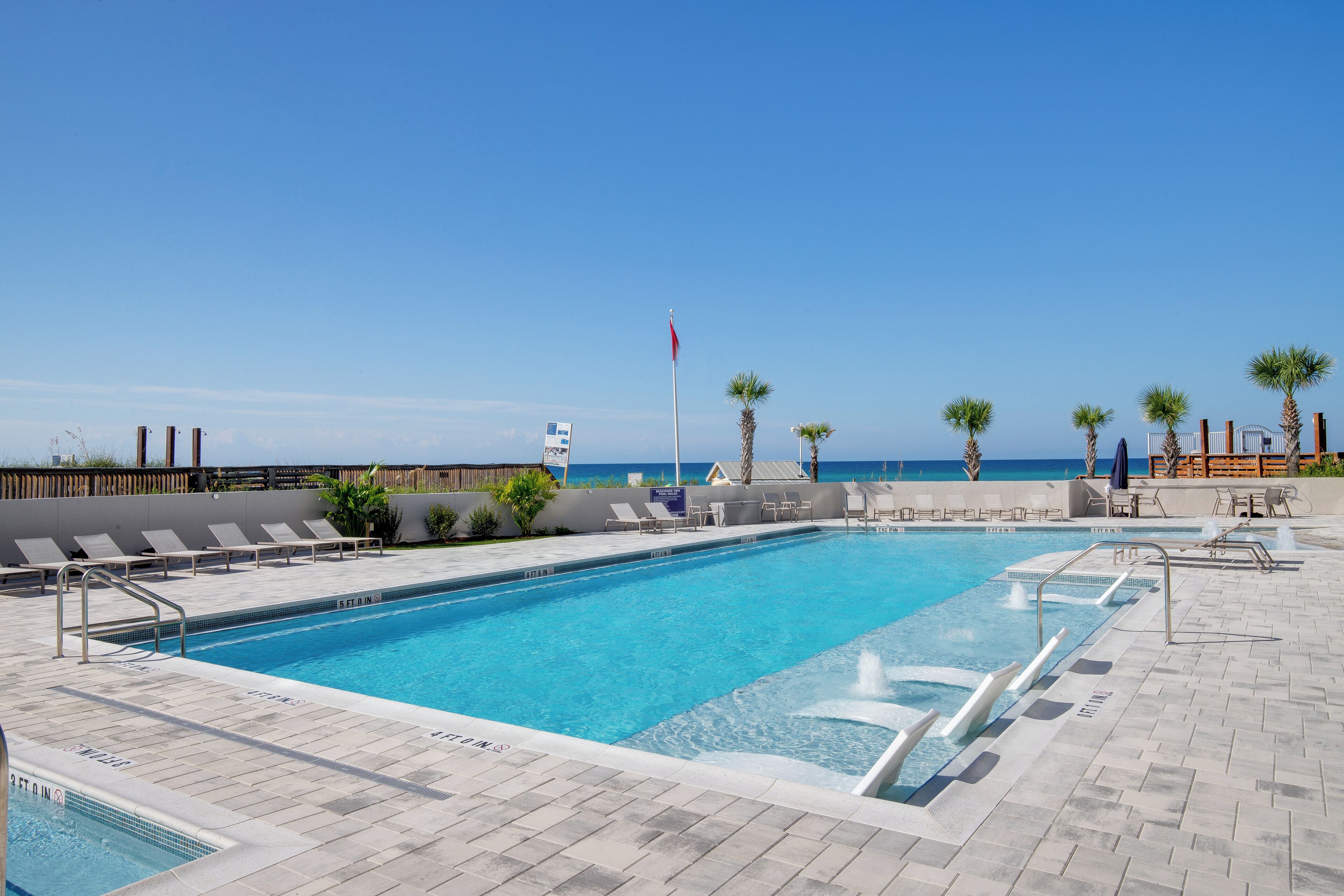 Ein Poolbereich mit klarem, blauem Wasser, Liegestühlen und Meerblick.