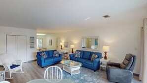 A living room with two blue sofas, a glass coffee table, a white rocking chair, a brown leather armchair, and a white side table with lamps. - Atlantic Breeze #5 2 bedrooms, 2 bathrooms (Jekyll Island)
