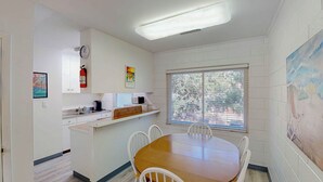 A small, clean room with a wooden table and white chairs, a window with blinds, a microwave, a sink, and a fire extinguisher. - Atlantic Breeze #5 2 bedrooms, 2 bathrooms (Jekyll Island)