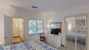 A bedroom with a bed, a dresser, a chair, a television, and a mirror. - Atlantic Breeze #5 2 bedrooms, 2 bathrooms (Jekyll Island)