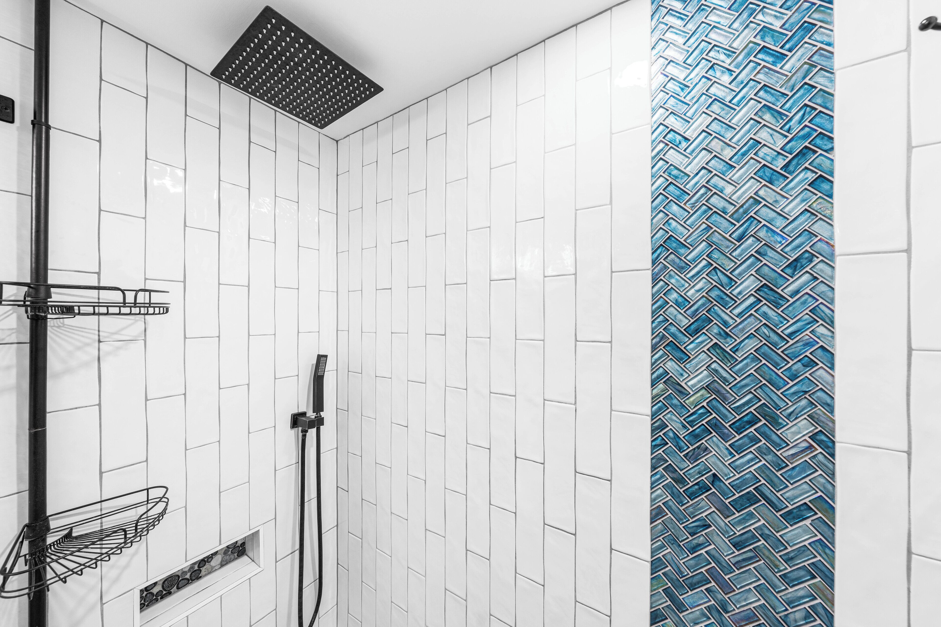 Un espace douche avec des murs recouverts de carreaux blancs, un motif de carreaux bleus décoratif et un receveur de douche en métal.