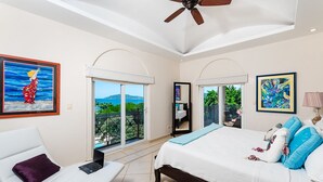 A bedroom with a bed, a laptop on a chair, a ceiling fan, and a balcony with a view. - Matapalo 606♆ Amazing Ocean views on the center of town ♆ (Tamarindo)