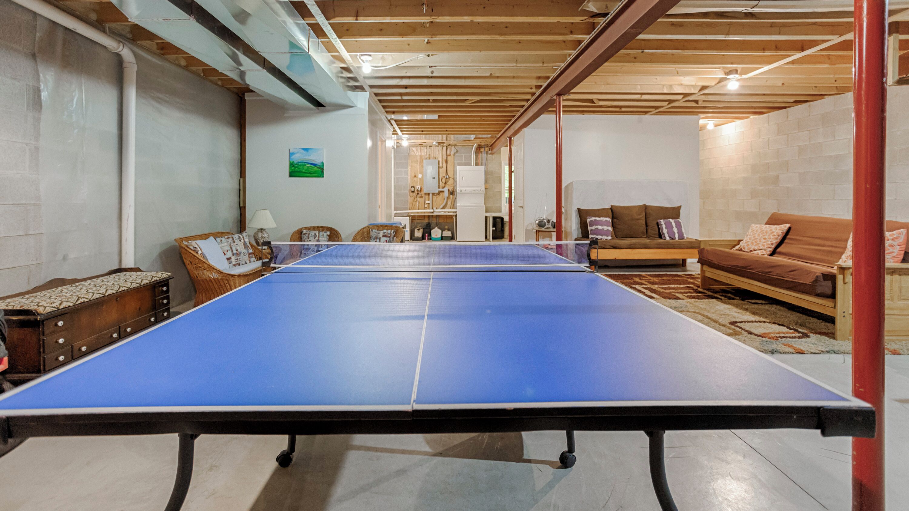 A room with a ping pong table, a sofa, and a wooden ceiling.