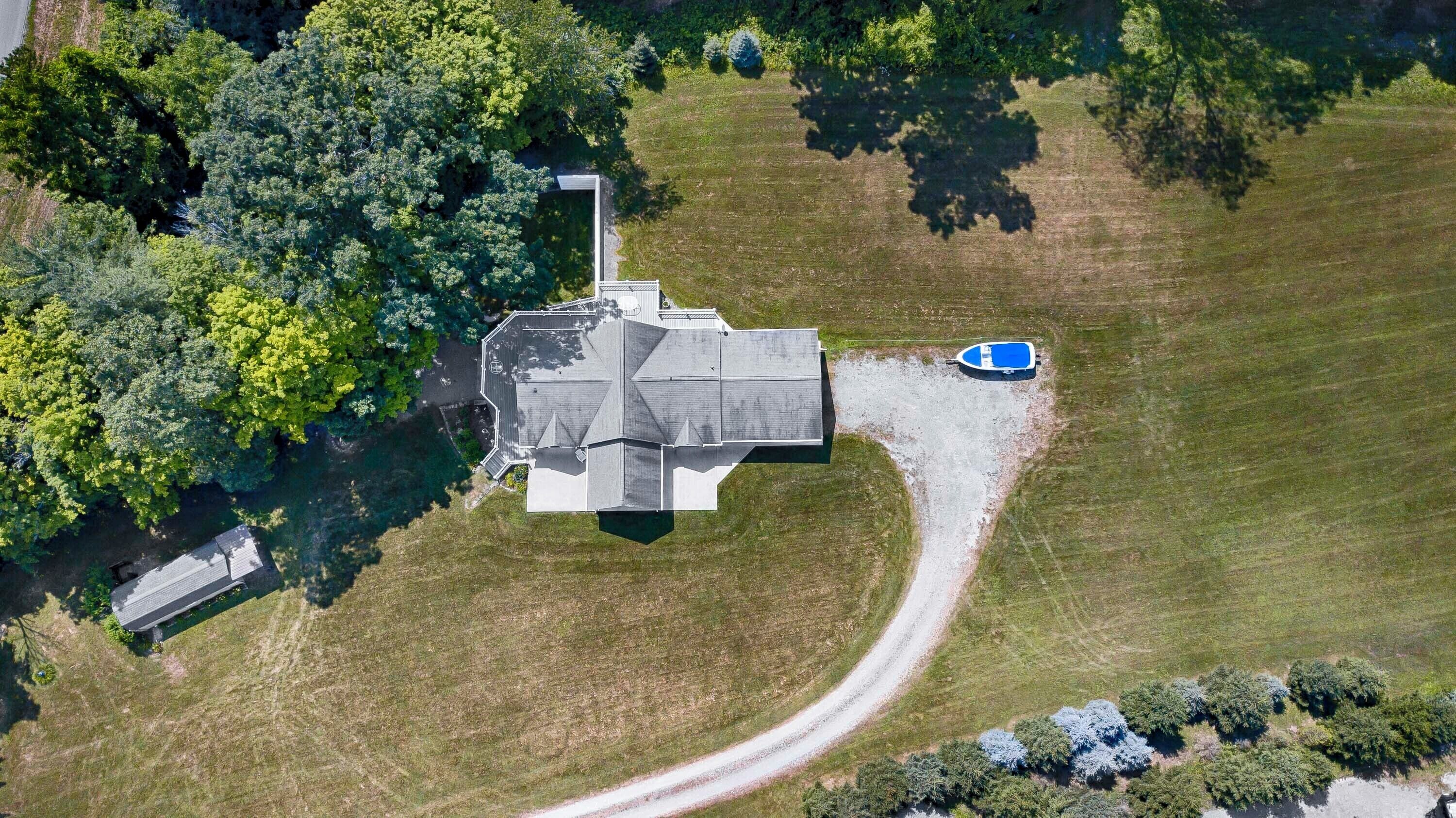 An aerial view of a large, modern house with a unique octagonal shape, surrounded by lush greenery and a small swimming pool.